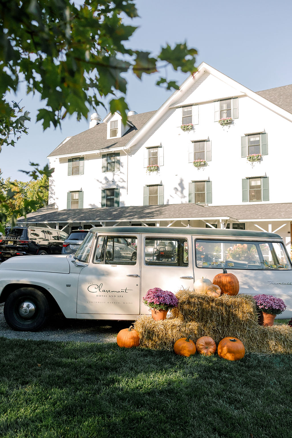 a white car with pumpkins and hay bales in front of a white house