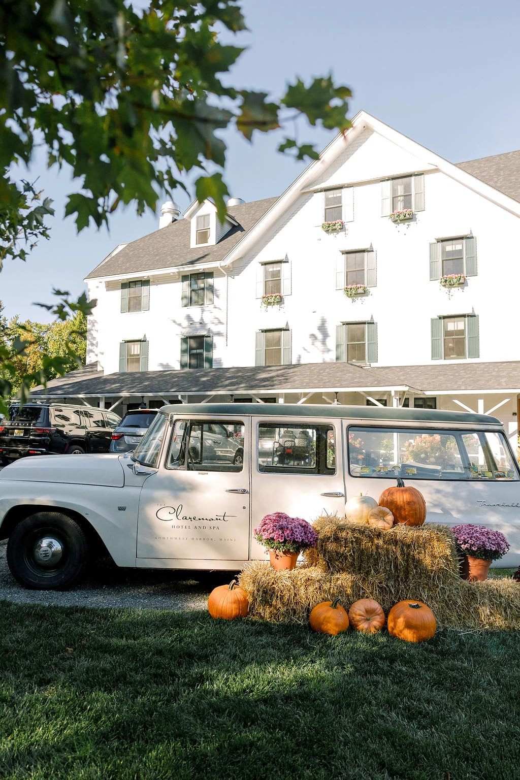 a white car with pumpkins and hay bales in front of a white house