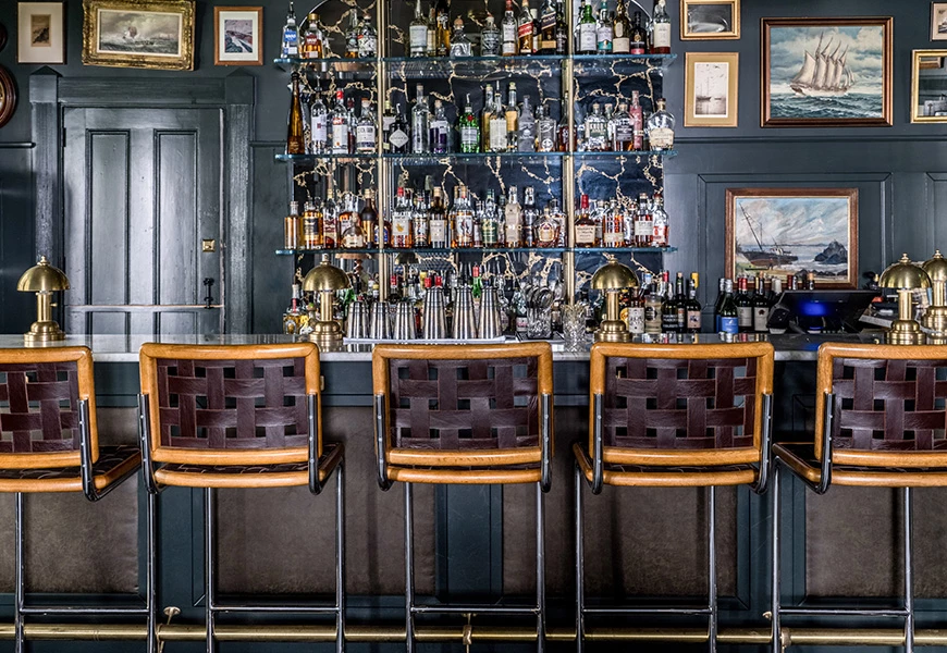a bar with a row of chairs and a shelf with bottles
