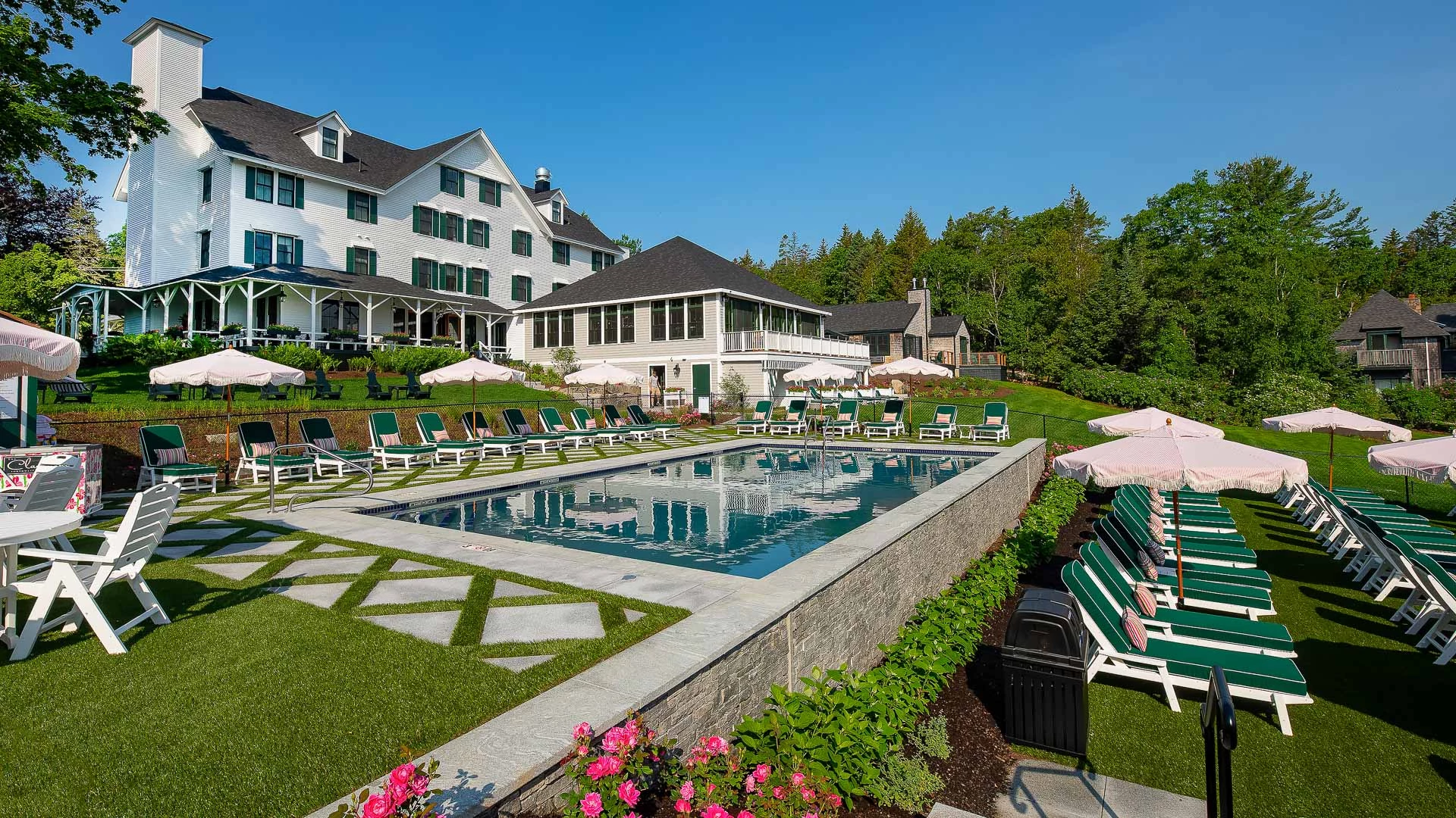 a pool with chairs and lawn chairs in front of a white house