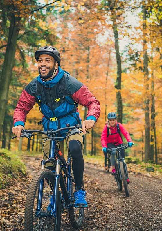 a man and woman riding bikes on a trail in the woods