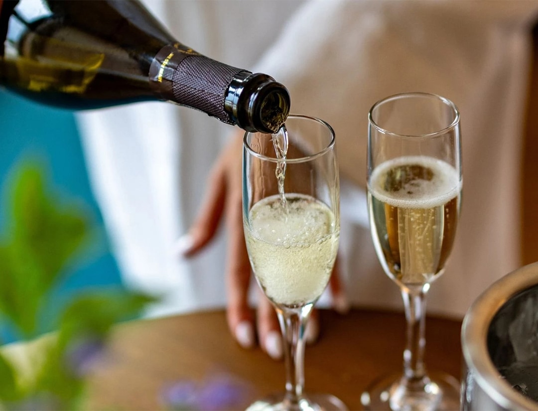 a person pouring champagne into two glasses