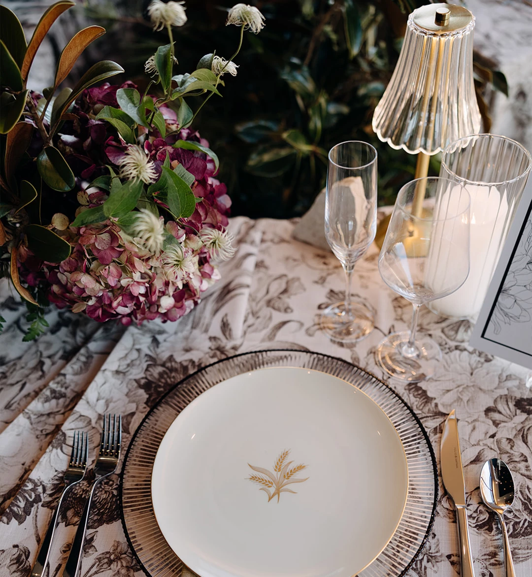 a table with a plate and glasses and a vase of flowers