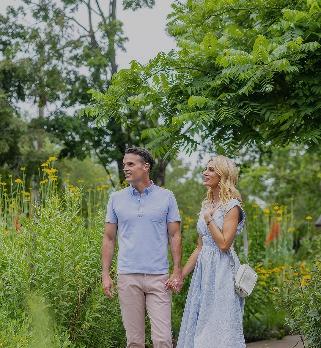 a man and woman holding hands and walking in a garden