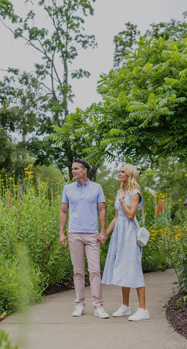 a man and woman holding hands and walking in a garden