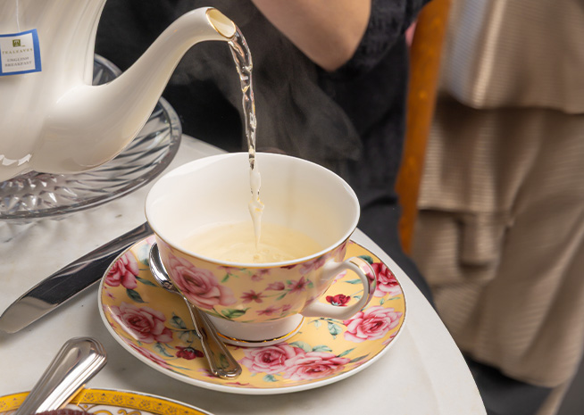 a teacup and saucer with a teapot pouring liquid into it