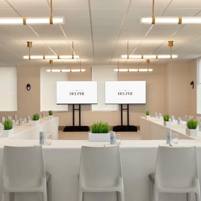 A well-lit meeting room with white tables, chairs, and screens