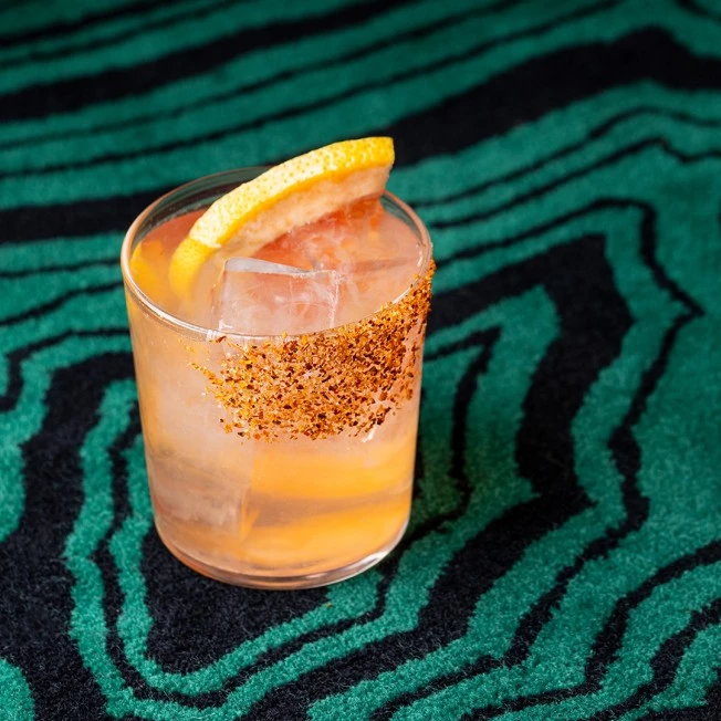 a cocktail with an orange slice and spices on a green and black background