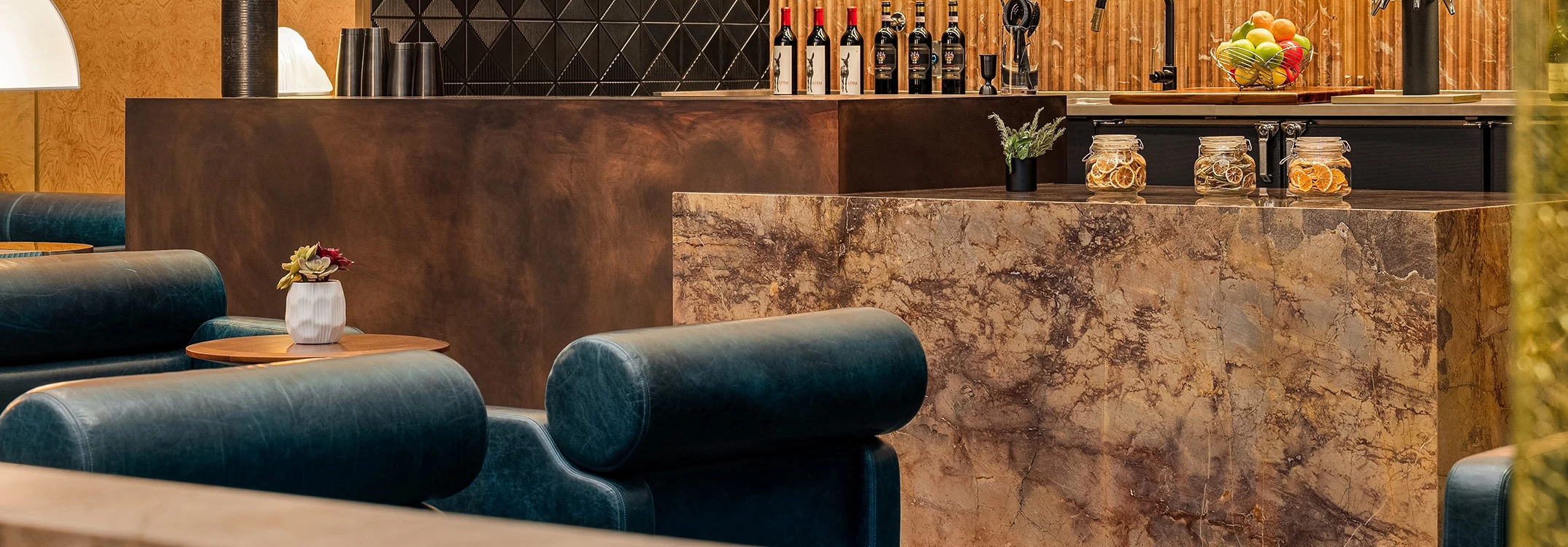 A luxurious bar area with a marble counter, blue leather chairs, and wine bottles on display.