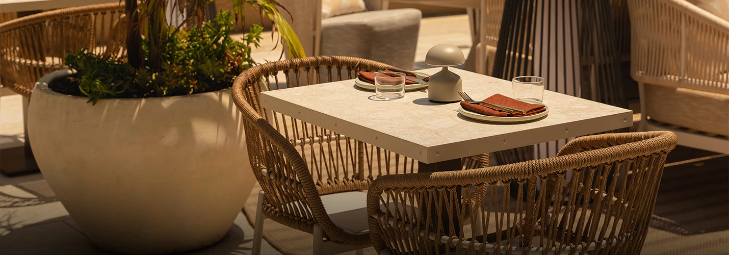 A cozy outdoor dining area with a marble table, wicker chairs, and a potted plant.
