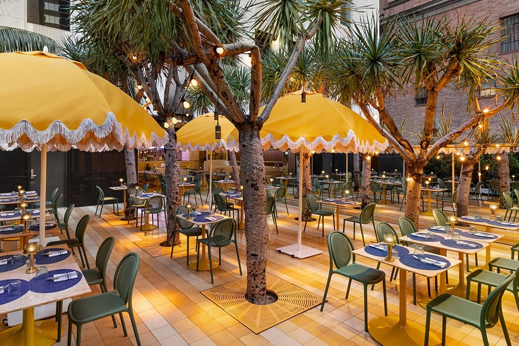 a restaurant patio with yellow umbrellas, palm trees, and string lights