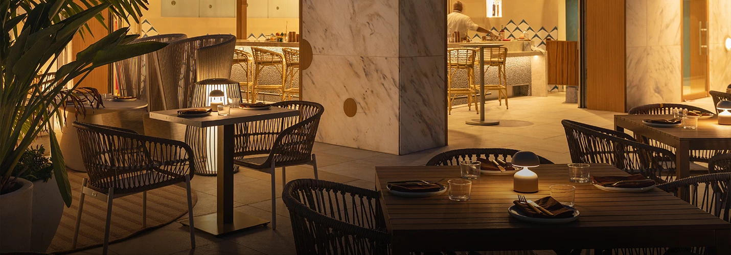 A restaurant dining area with tables set for dinner, warm lighting, and plants.