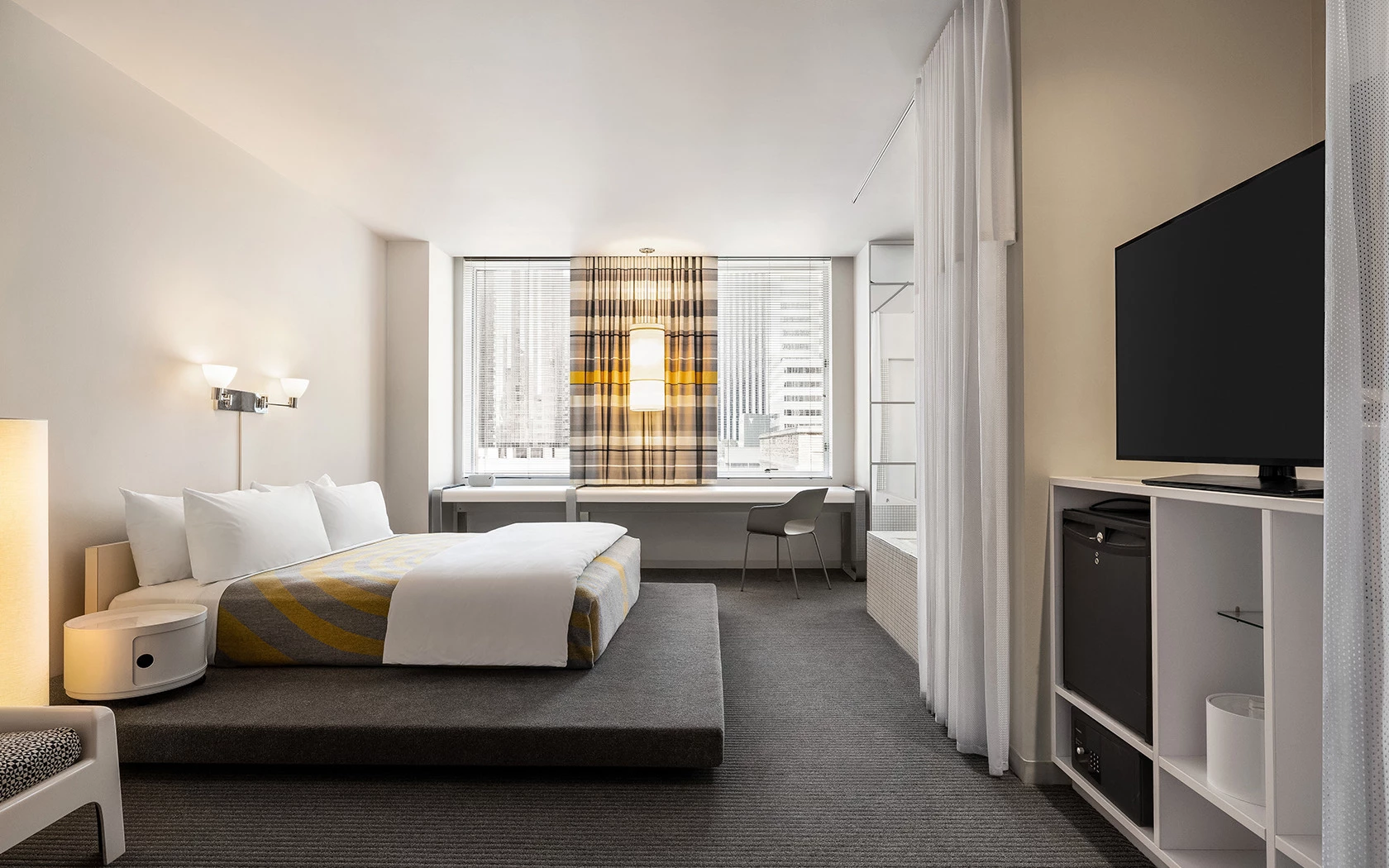 A wide view of a hotel room with a bed, TV, window, and desk.