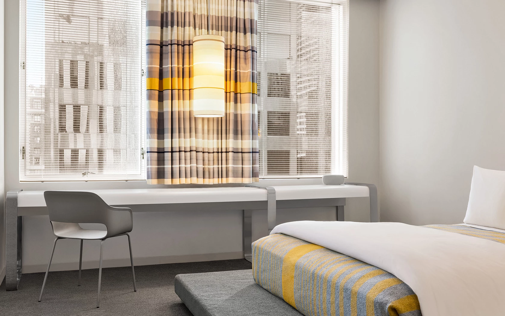 A hotel room with a bed, desk, and window