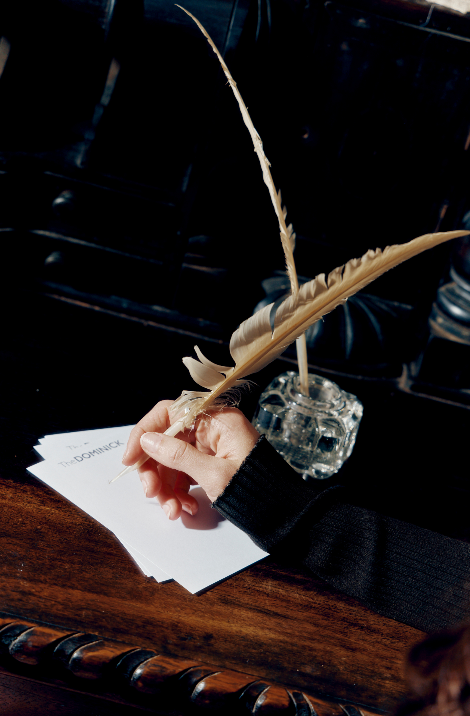 a hand holding a feather pen and a glass inkwell