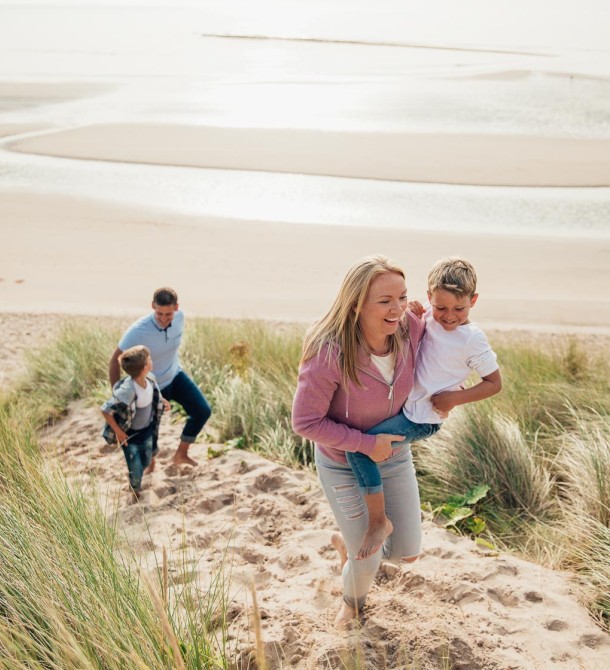 a woman holding a child and a man playing on sand