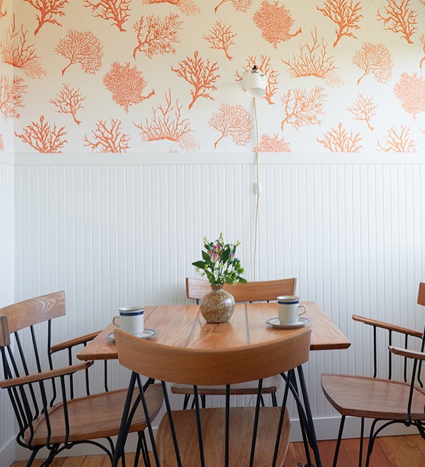 A wooden table with two cups of coffee and the sun shining  in from the right.