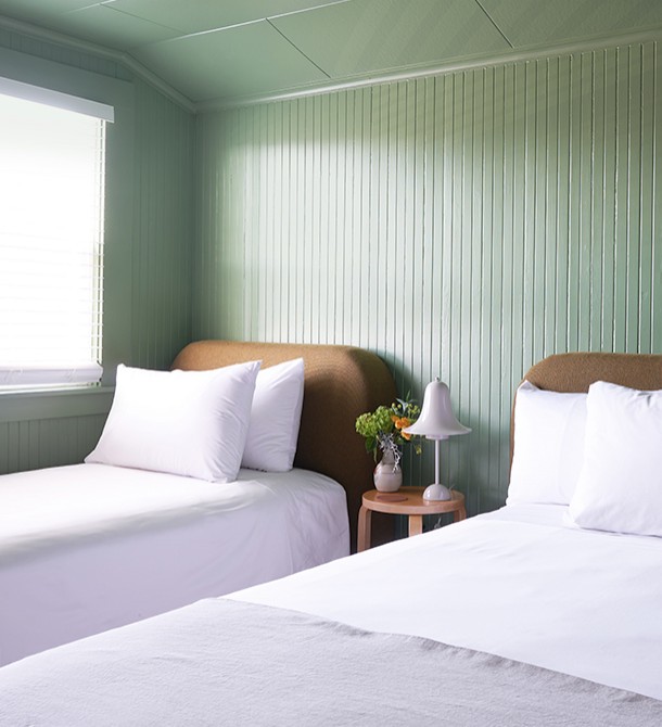 The sun shining into a light green colored bedroom with two beds and a small wooden table.
