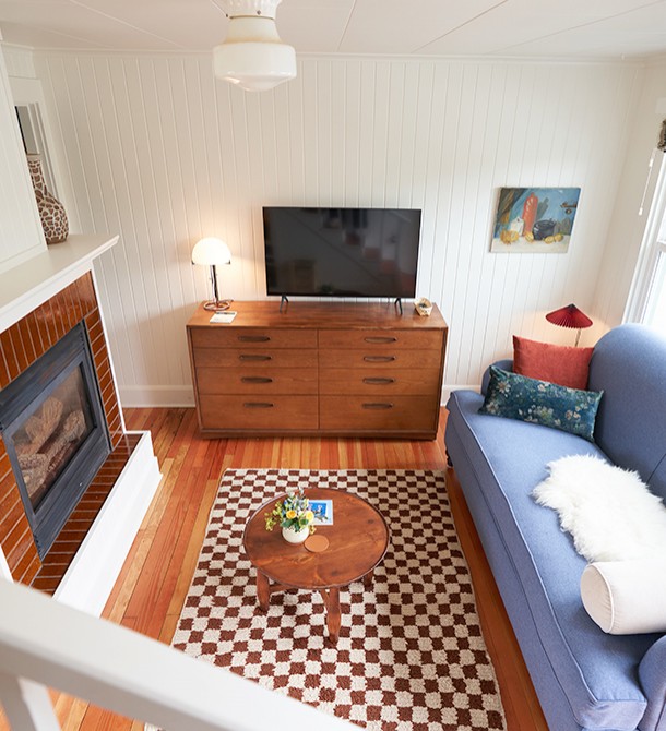 A view from the stairs down to the living room with a flat panel television and a fireplace.