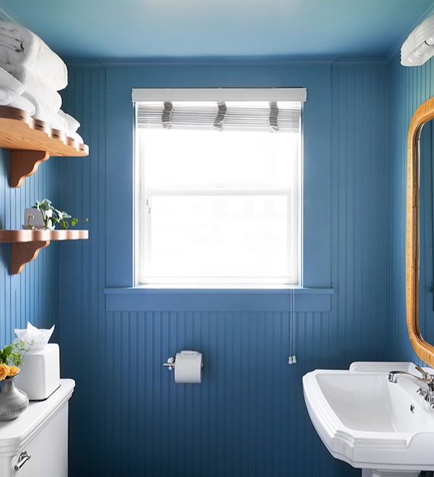 A dark blue colored bathroom with white sink and wooden shelves.