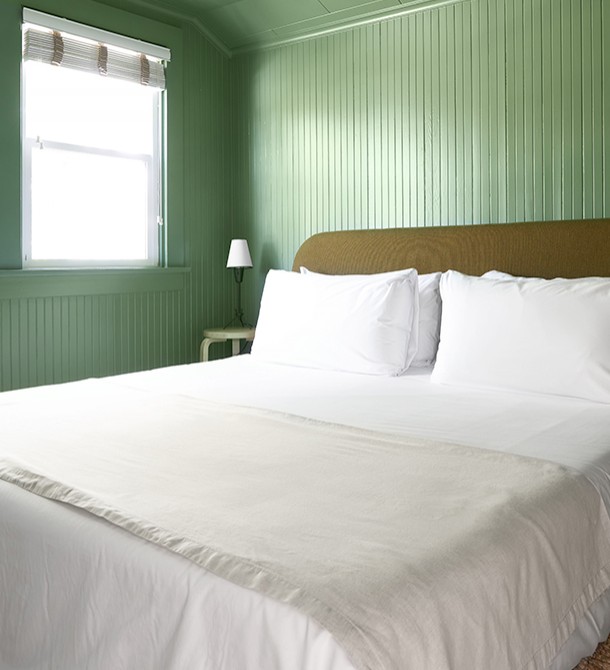 A bed with an olive colored headboard in a light green colored room.