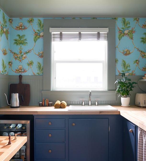 A kitchen with tropical designed wallpaper and the sun shining in from the window.