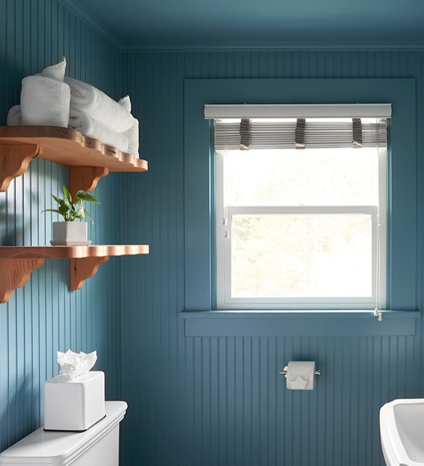 A light blue colored bathroom with wooden shelves and the sun shining in from the window.