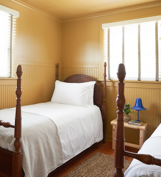 Two wooden beds in a room with the sun shining in from the windows.