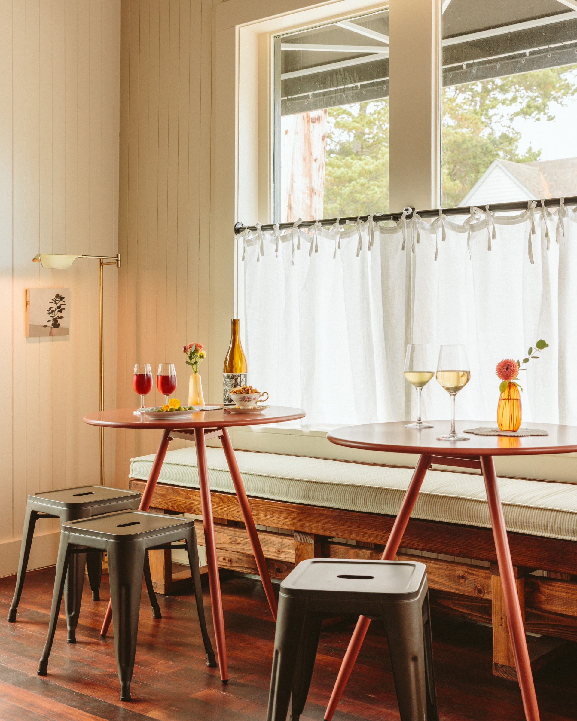 a table with wine glasses and stools in a room with windows