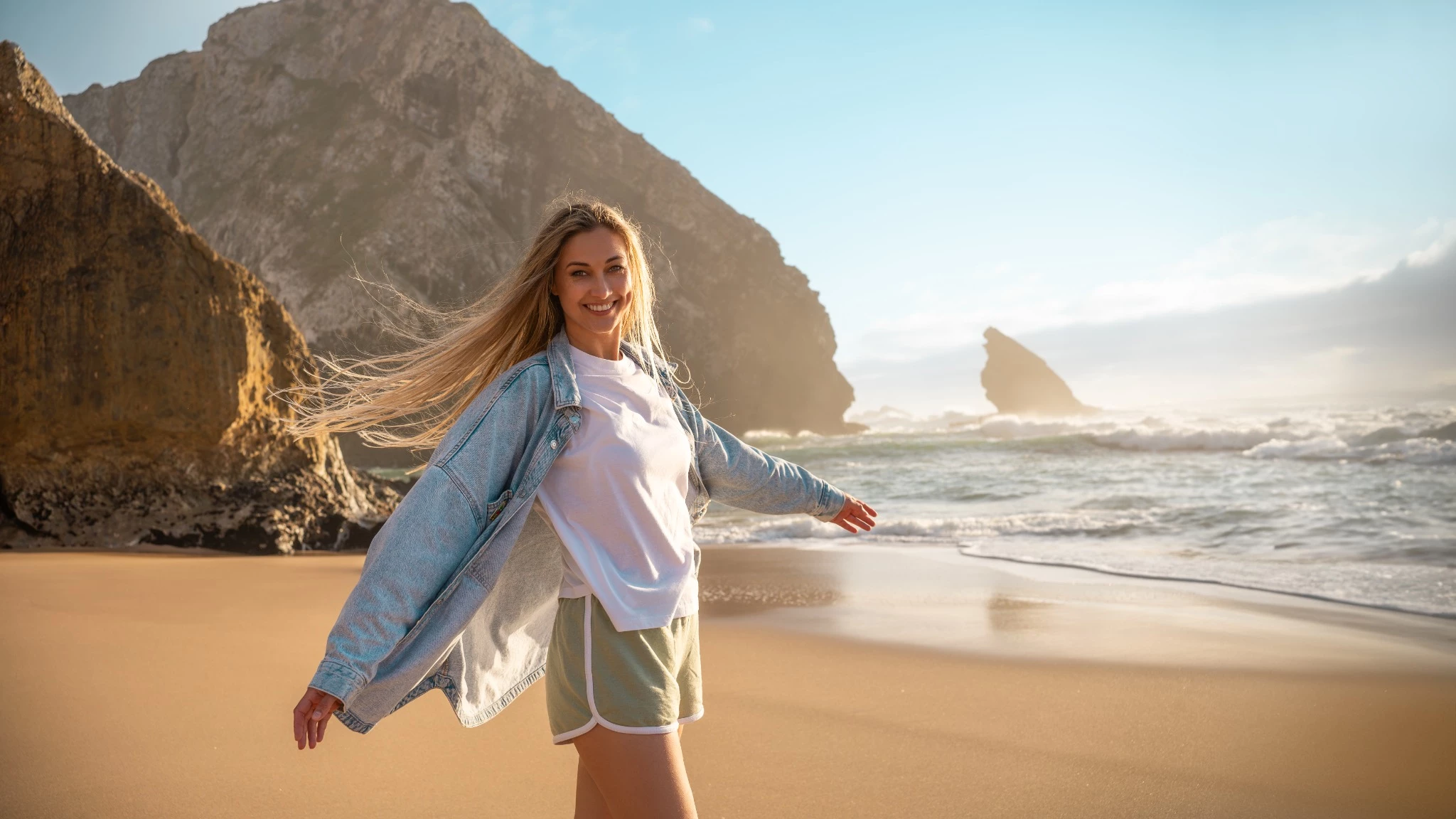 a woman standing on a beach with waves and a mountain in the background