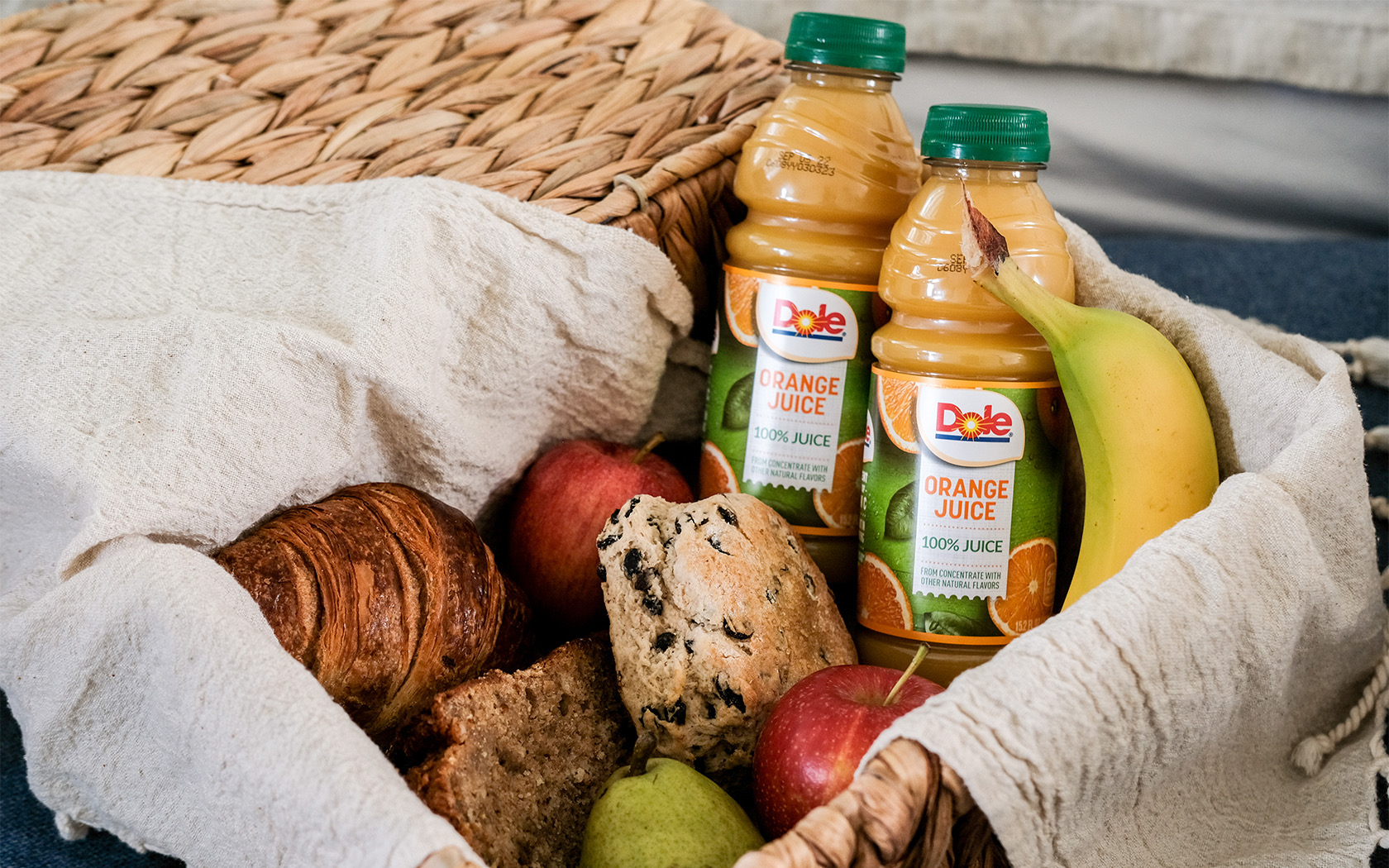 A basket filled with breakfast foods such as fresh fruit, muffins, and orange juice.