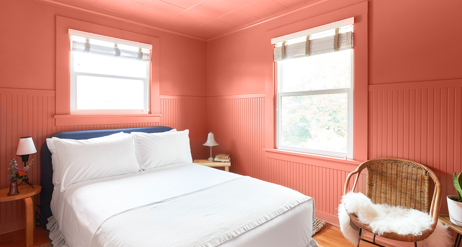 A peach colored bedroom with a bed and chair.