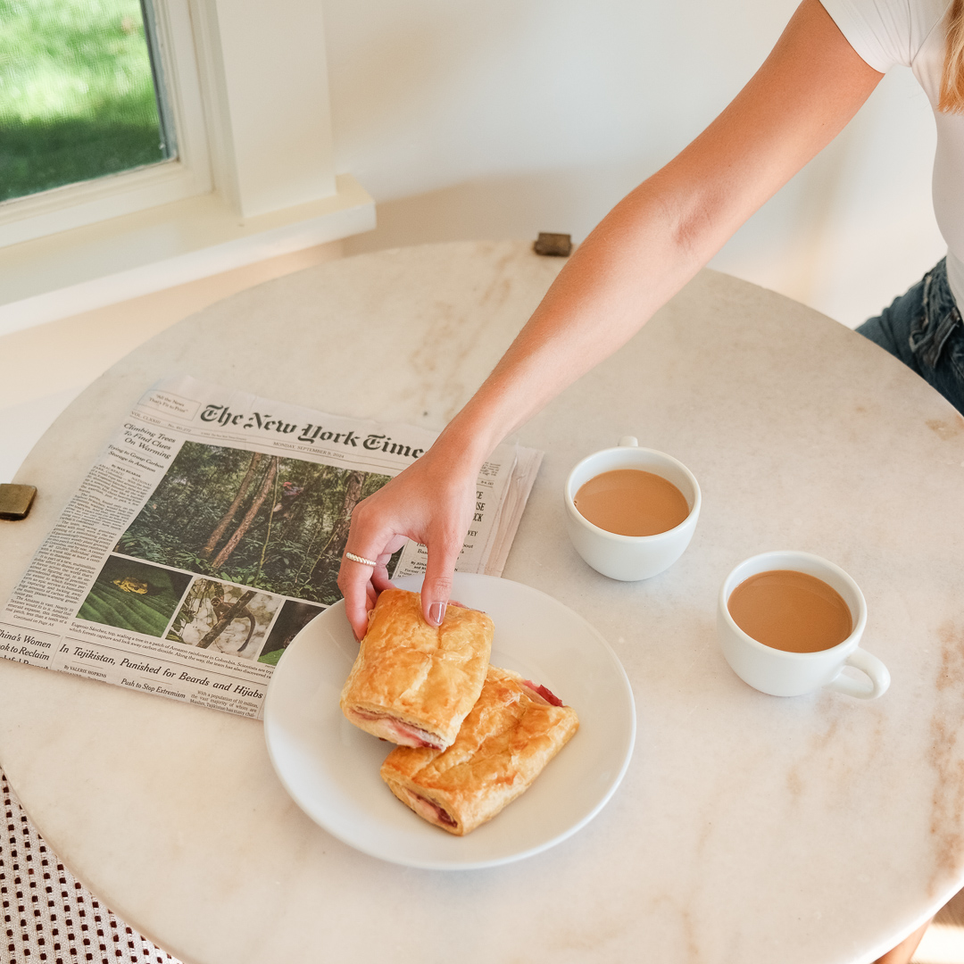 a woman holding a sandwich on a plate next to cups of coffee