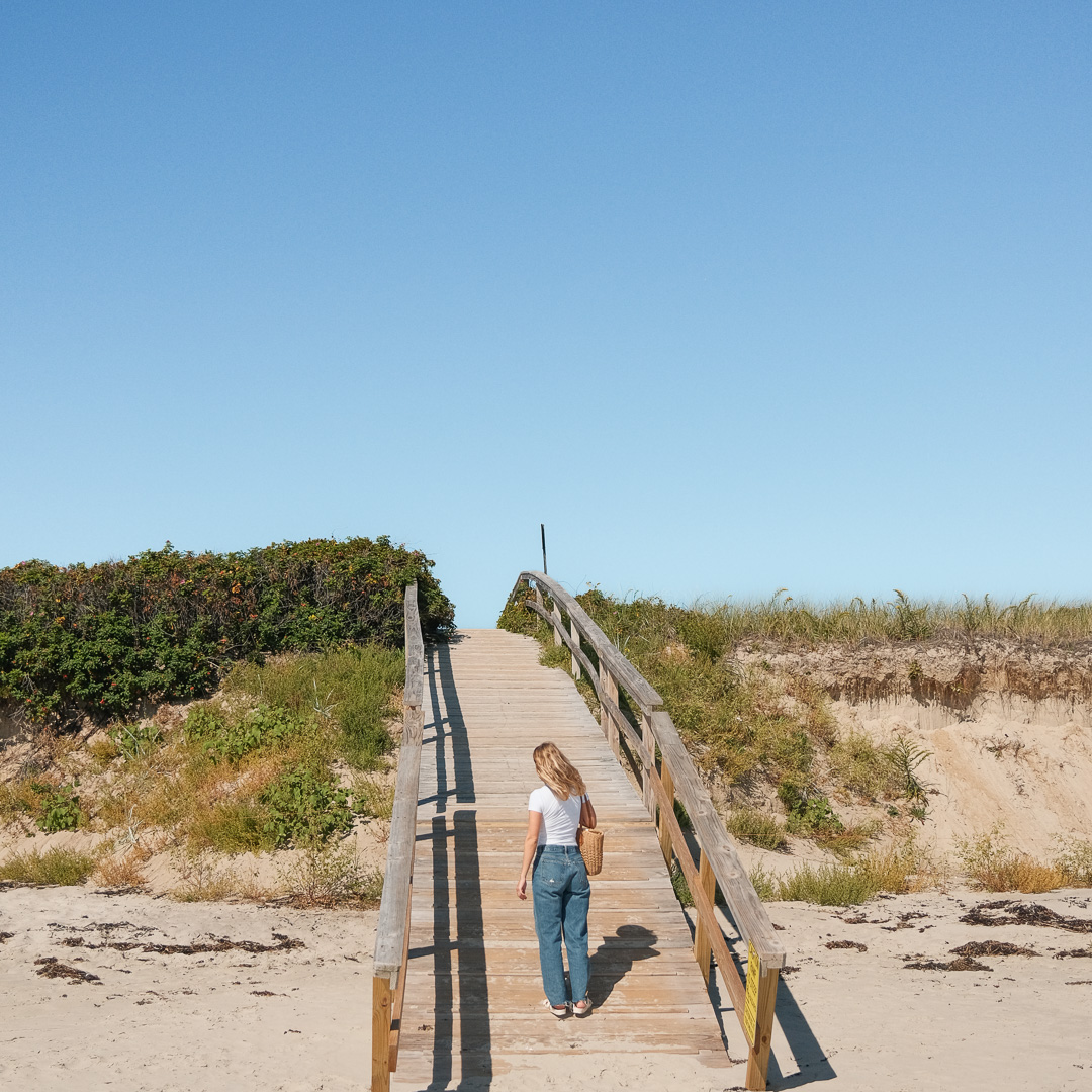 a woman walking on a wooden bridge over a beach