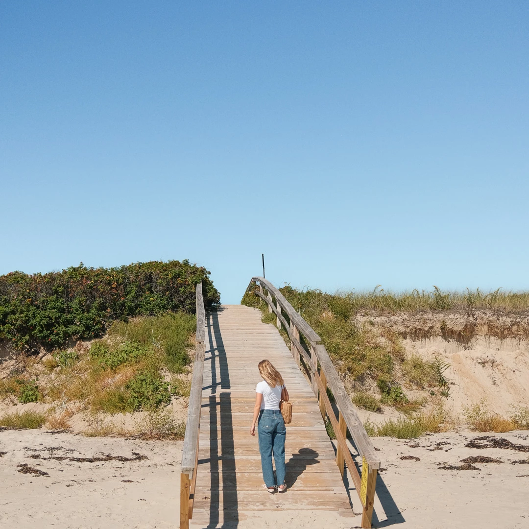 a woman walking on a wooden bridge over a beach