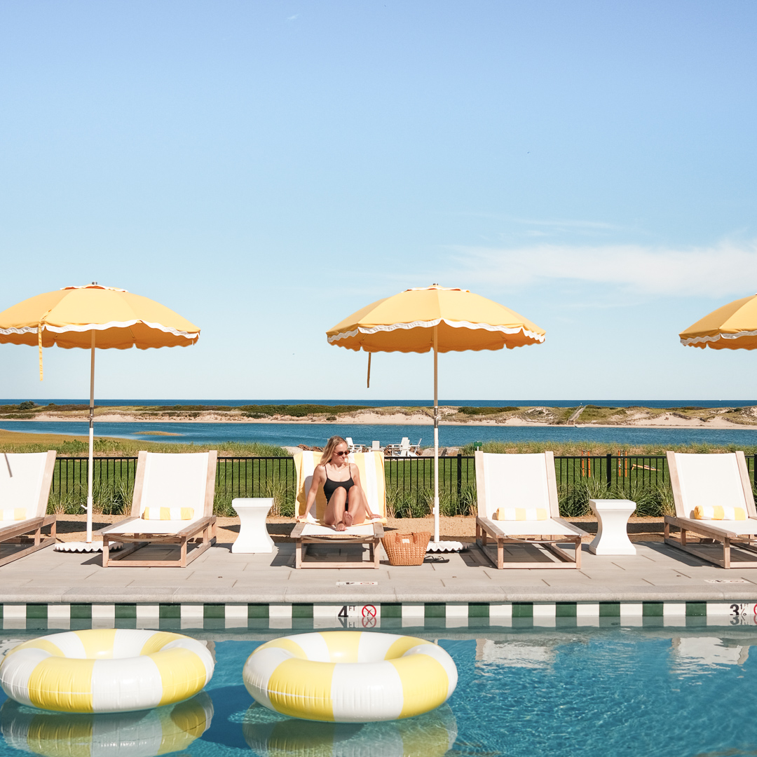 a woman sitting on a chair by a pool with yellow umbrellas