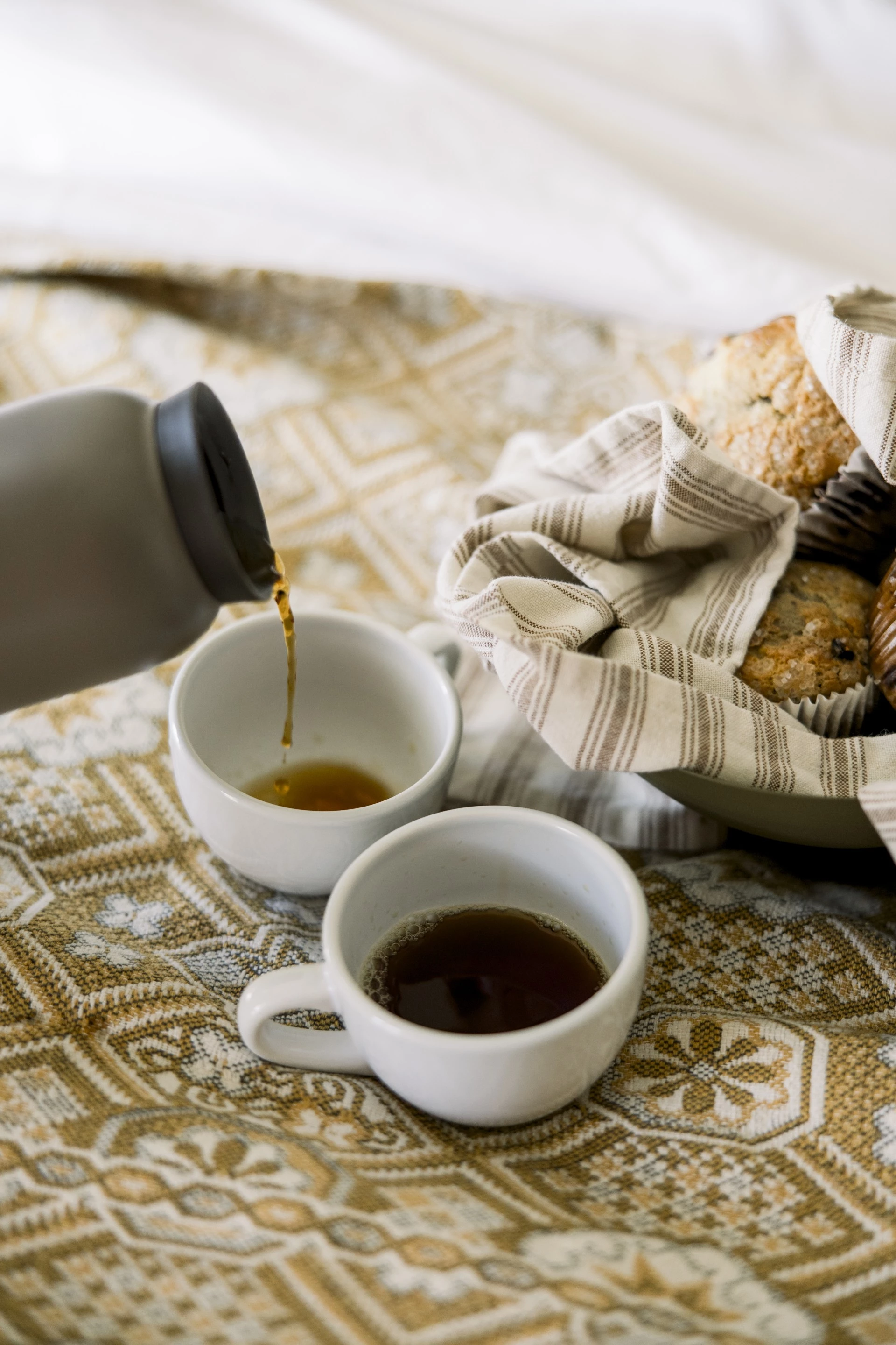 a close-up of two cups of coffee and muffins on a bed