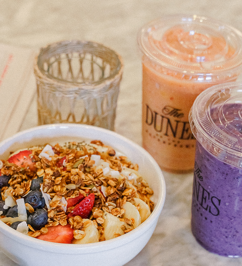 a bowl of granola and fruit next to two plastic cups