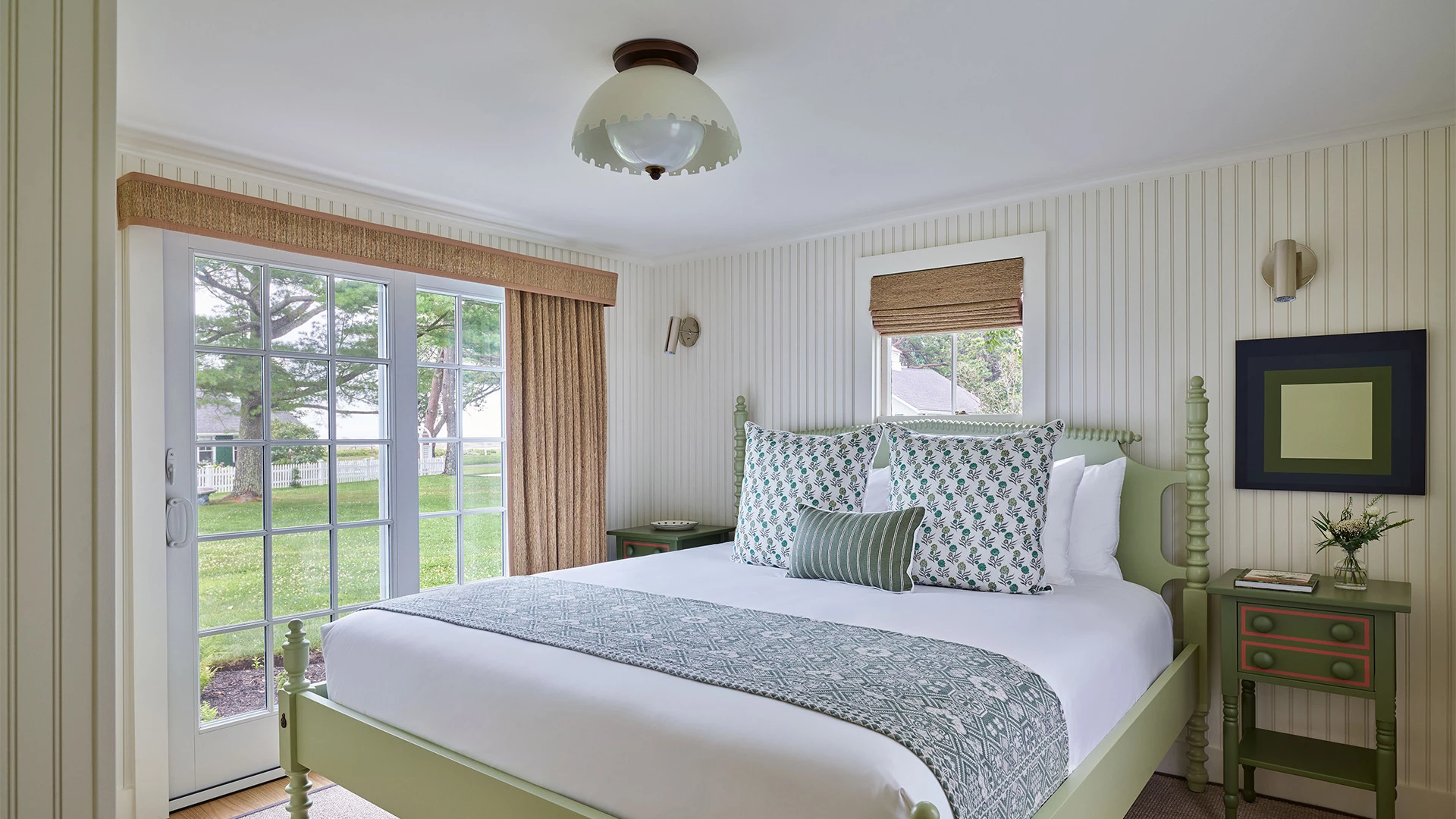 A neatly made bed with green and white bedding in a room with white walls and a window.
