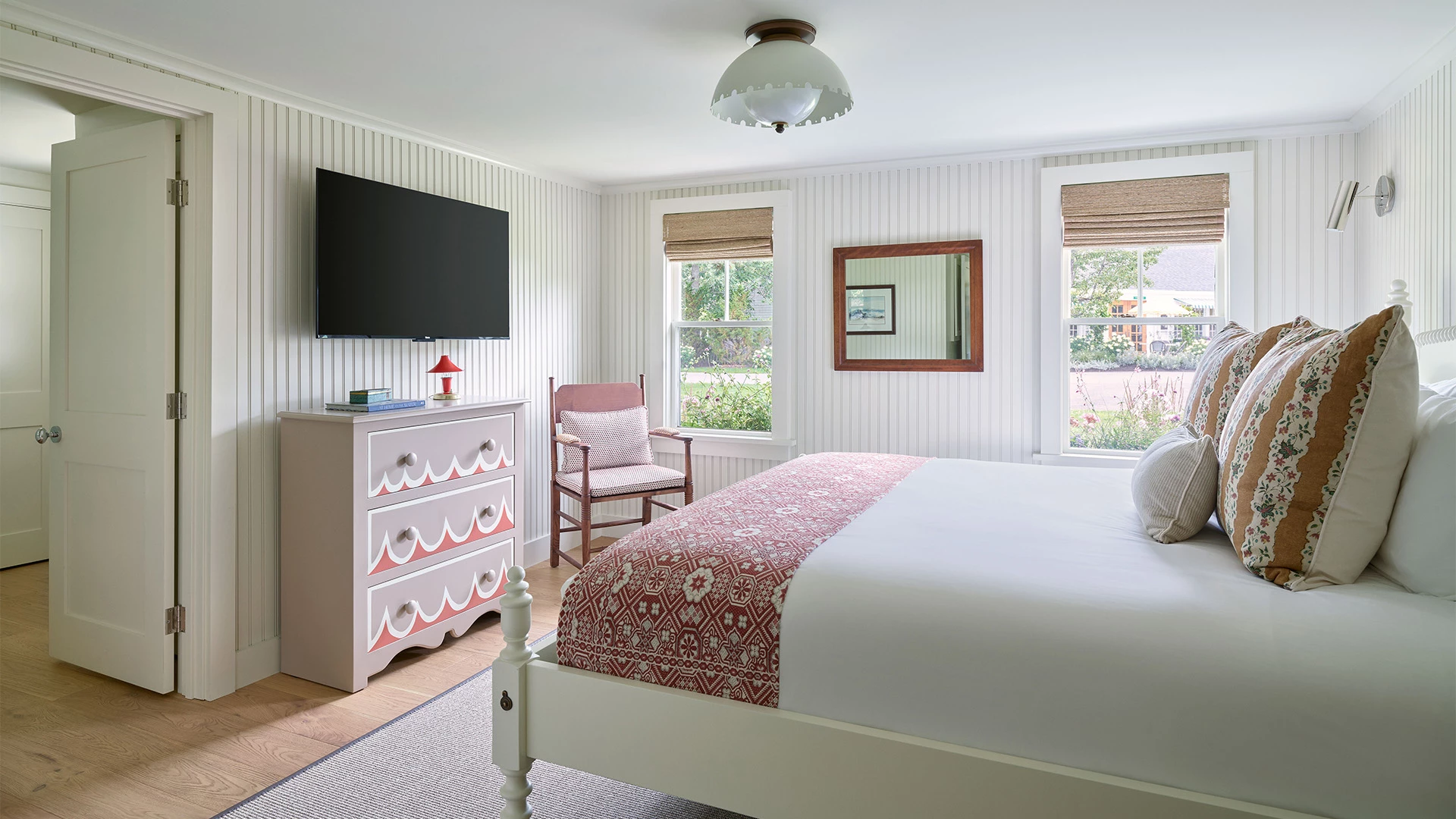 A bright and airy hotel room with a white bed, pink accents, and a TV on the wall.