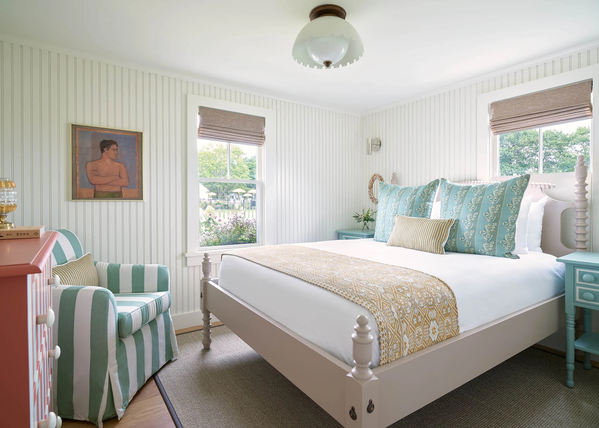 A white bedroom with a large bed, a striped chair, and a dresser.