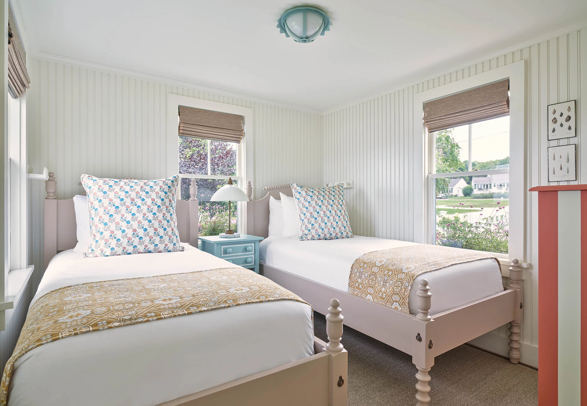 A bright and airy room with two beds, two windows, and a blue nightstand.