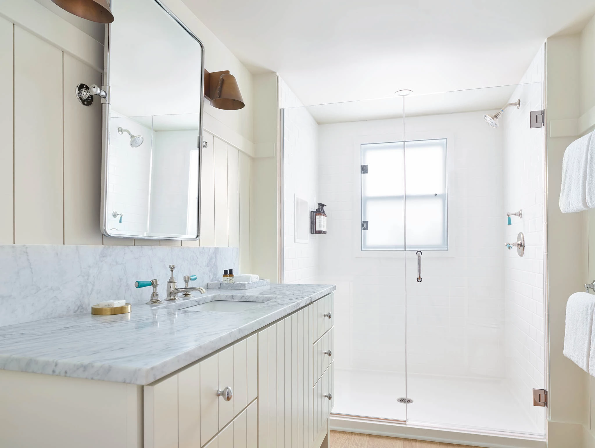 A clean and modern bathroom with a marble countertop, glass shower door, and large mirror.