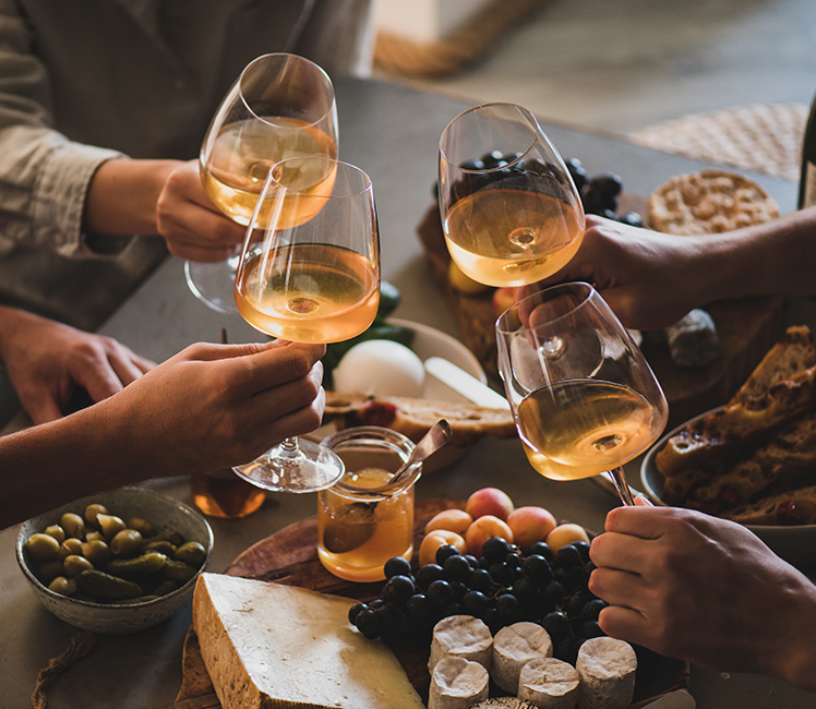 close up of four glasses of white wine being clinked over a charcuterie board