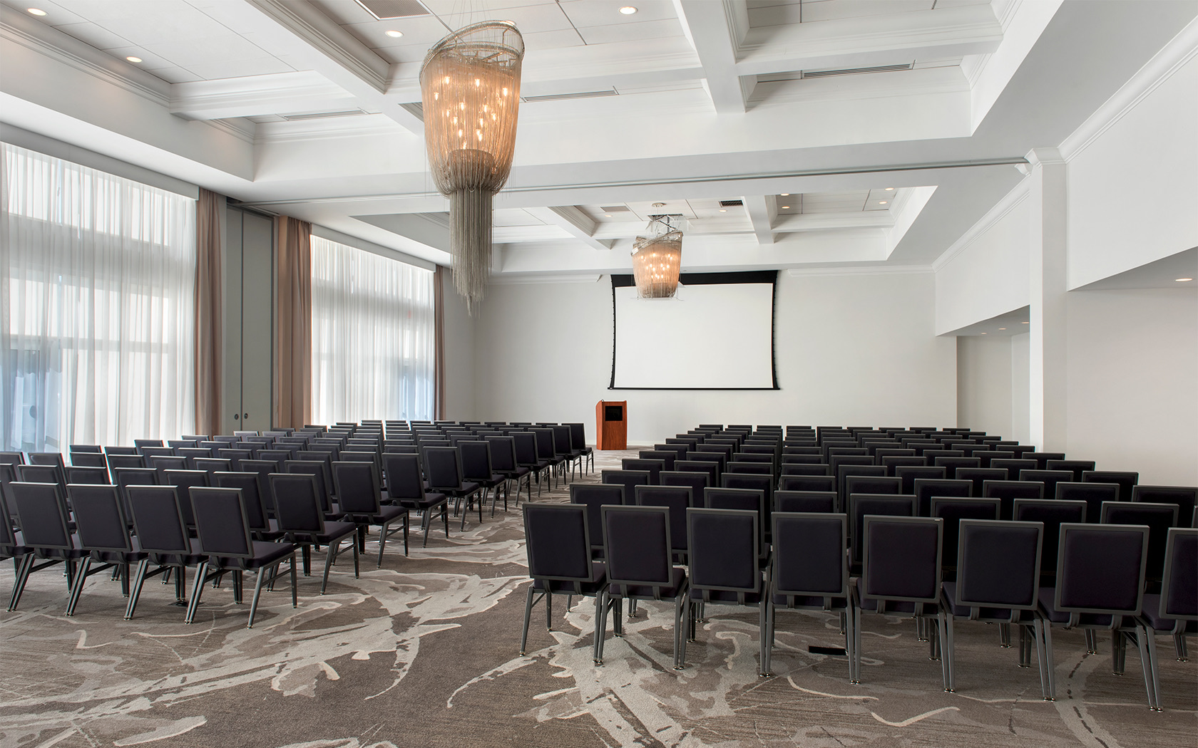 two large chandeliers in a meeting space with many chairs and a projection screen