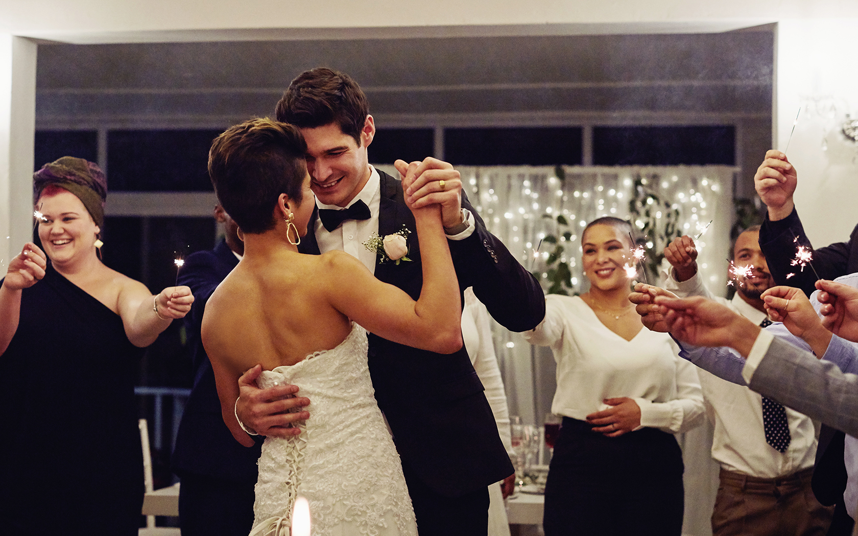 smiling people holding lit sparklers while standing around a bride and groom
