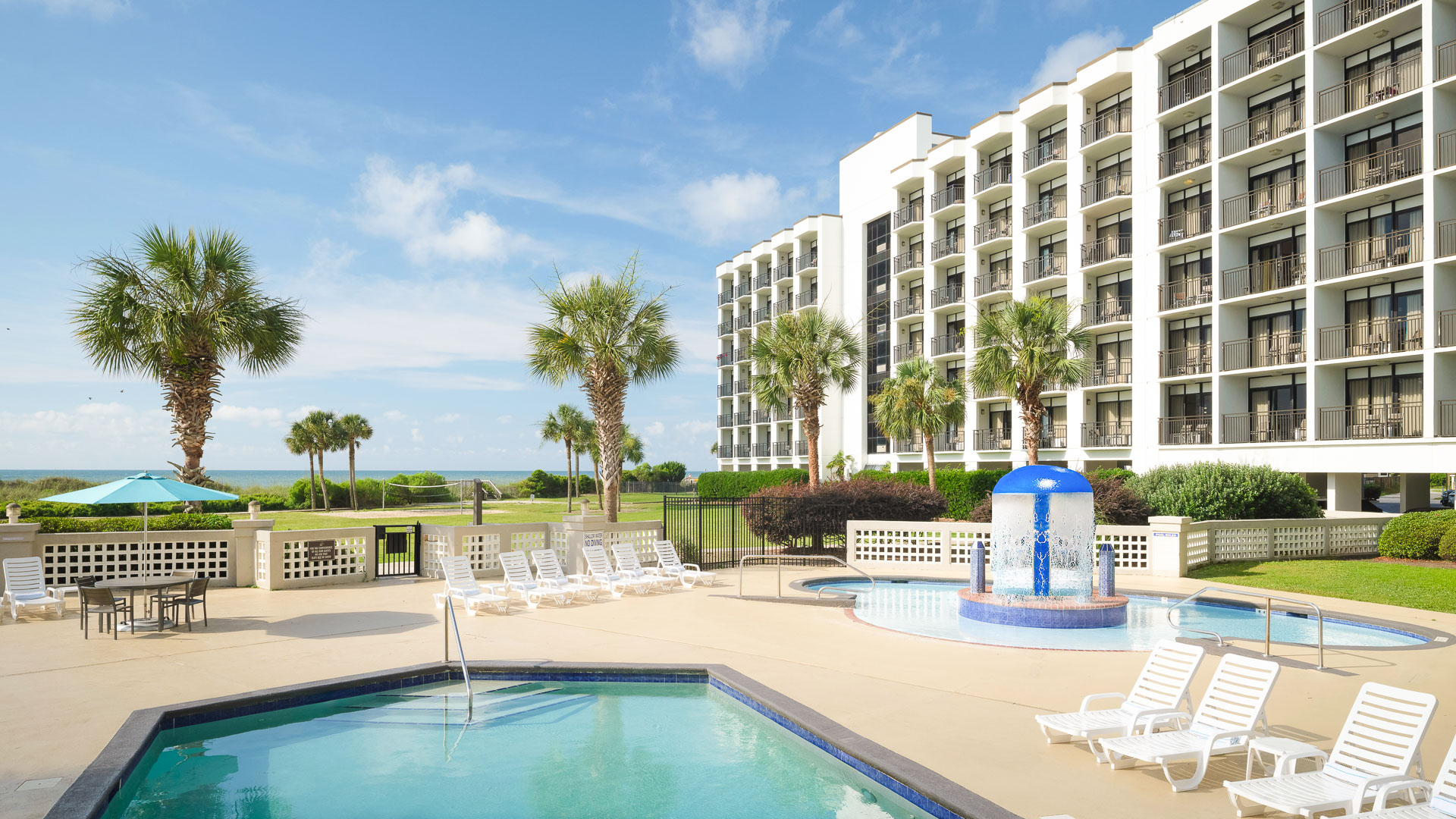 a pool with a fountain and palm trees in front of a building