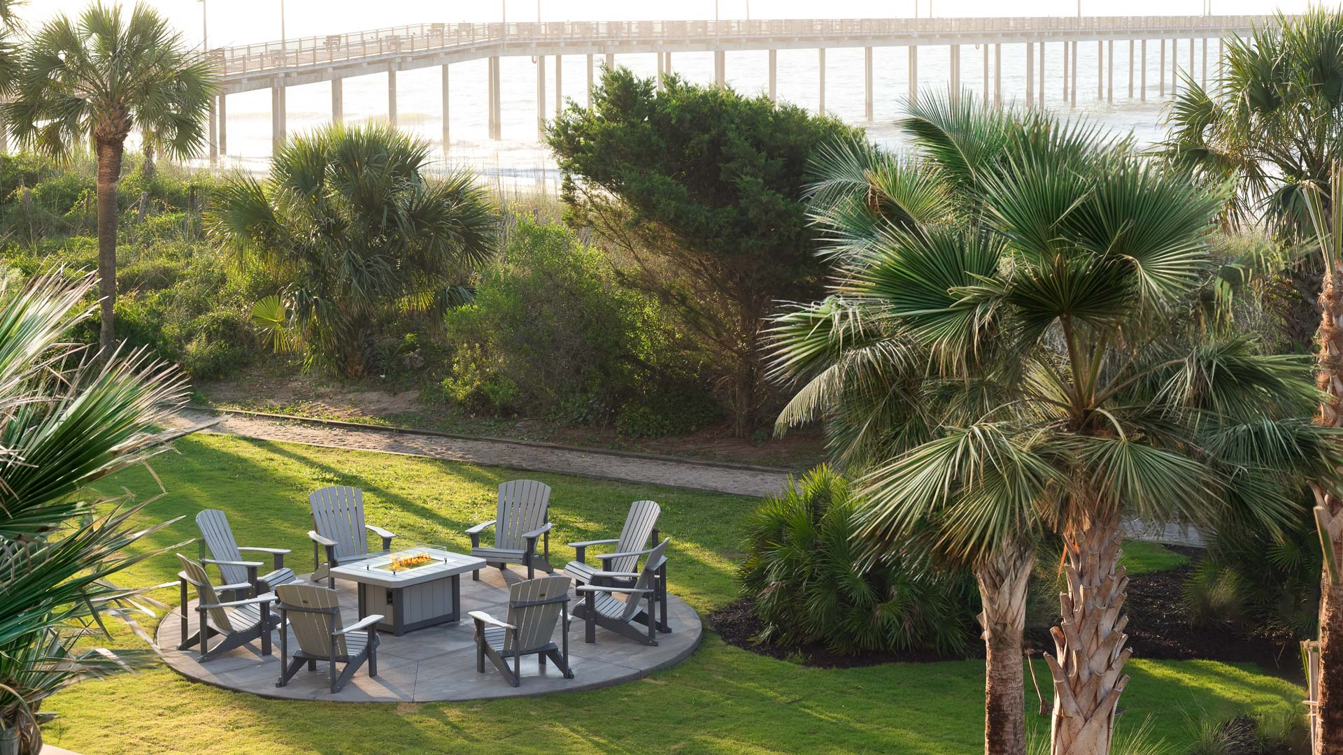 a patio with a table and chairs in a grassy area with a pier in the background