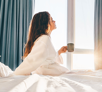 a woman sitting on a bed holding a cup