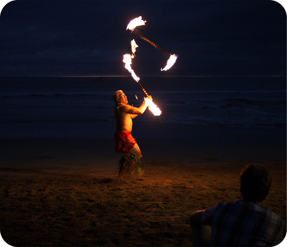 a man holding fire sticks on a beach